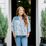 Woman with red hair wearing a quarter-sleeve top with blue Santa toile graphics and blue embroidery on shoulders and chest. Model paired this top with denim jeans.