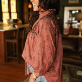 Woman with dark hair standing in a side profile position wearing the Jane Top in a lifestyle scene. The focal point of this image is the cowgirl graphics as well as embroidery along shoulders. The model paired this top with light-wash denim jeans. 