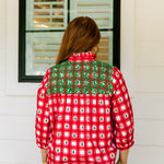 Woman with red hair wearing a quarter-sleeve top with red plaid graphics and green embroidery. Model paired this top with light-wash denim jeans. 