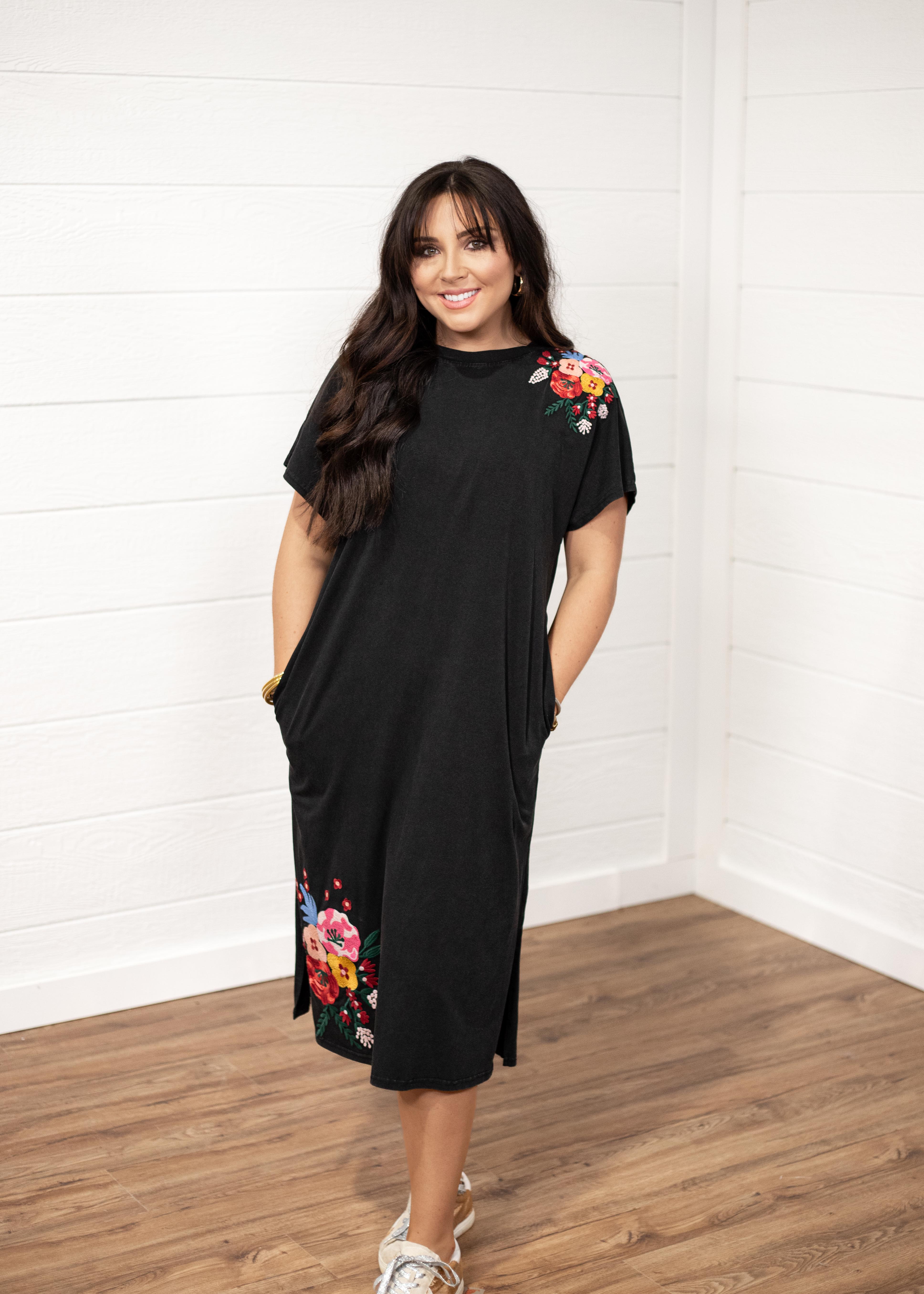 Woman with dark hair standing in a front profile position wearing the Jo Dress against a white background. The focal point of this image is the embroidery on sleeve and bottom of dress. The model paired this dress with white and gold sneakers.
