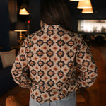 Woman with dark hair wearing a long-sleeve red, black, and yellow aztec top. The model paired light-wash denim jeans with this top.