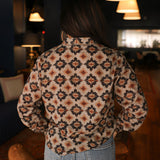 Woman with dark hair wearing a long-sleeve red, black, and yellow aztec top. The model paired light-wash denim jeans with this top.