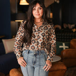 Woman with dark hair wearing a long-sleeve red, black, and yellow aztec top. The model paired light-wash denim jeans with this top.
