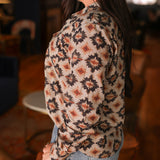 Woman with dark hair wearing a long-sleeve red, black, and yellow aztec top. The model paired light-wash denim jeans with this top.