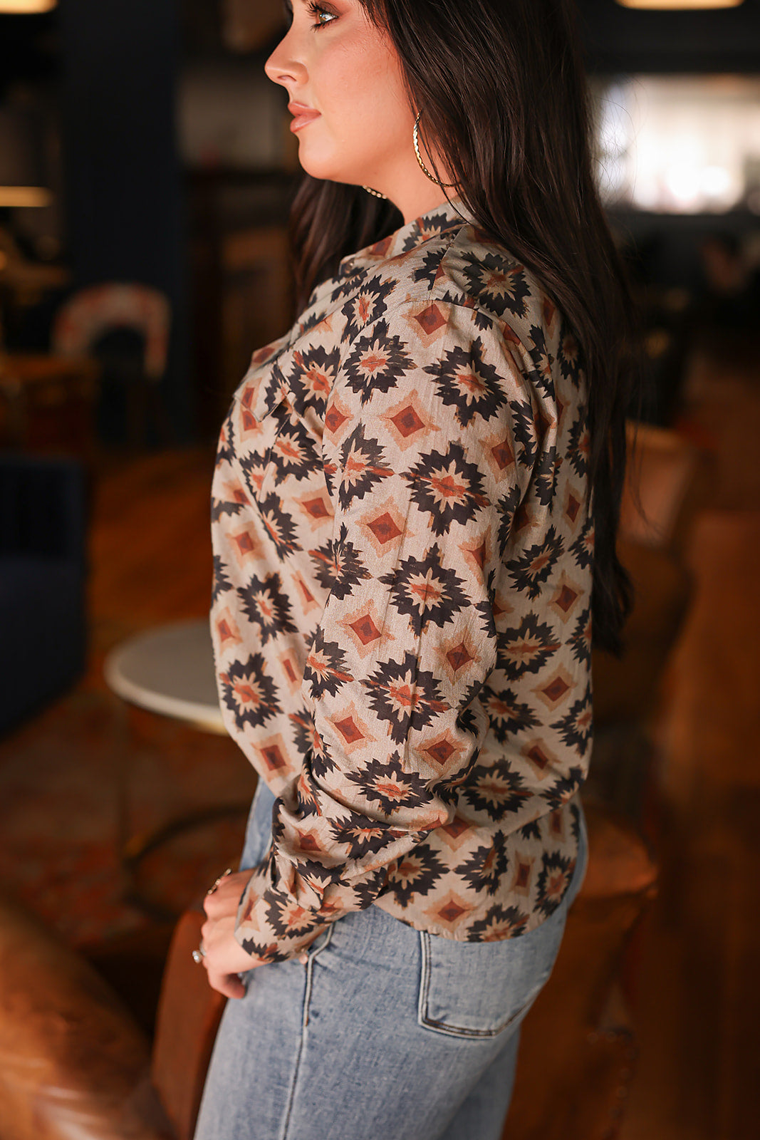 Woman with dark hair wearing a long-sleeve red, black, and yellow aztec top. The model paired light-wash denim jeans with this top.