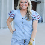Woman with blonde hair wearing a short-sleeve denim top with maroon floral embroidery on sleeves, and light-wash denim shorts. 