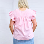 Woman with blonde hair standing in a back profile position wearing the Kinley Top against a white background. The focal point of this image is the gingham pattern on top as well as pleating and ruffle sleeves. The model paired this top with a light-wash denim skirt. 