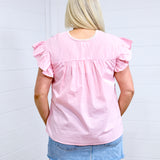 Woman with blonde hair standing in a back profile position wearing the Kinley Top against a white background. The focal point of this image is the gingham pattern on top as well as pleating and ruffle sleeves. The model paired this top with a light-wash denim skirt. 