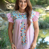 Woman with red hair standing in a front profile position wearing the Kinley Top in a lifestyle scene. The focal point of this image is the front embroidery as well as the ruffle sleeves. The model paired this top with dark-wash denim jeans.
