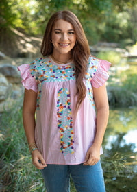 Woman with red hair standing in a front profile position wearing the Kinley Top in a lifestyle scene. The focal point of this image is the front embroidery as well as the ruffle sleeves. The model paired this top with dark-wash denim jeans.