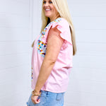 Woman with blonde hair standing in a side profile position wearing the Kinley Top against a white background. The focal point of this image is the embroidery on front of top and ruffle sleeve. The model paired this top with the light-wash denim skirt. 