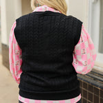 Woman with blonde hair standing in a back profile position wearing the Kodi Vest in a lifestyle scene. The focal point of this image is the cable knit pattern on back of sweater. The model paired this with dark-wash denim jeans and the Jesse Top.