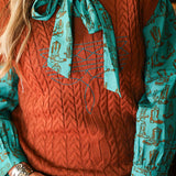 Woman with blonde hair standing in a front profile position wearing the Kodi Vest in a lifestyle scene. The focal point of this image is v-neckline and turquoise boot stitch. the model paired this top with dark-wash denim jeans. 