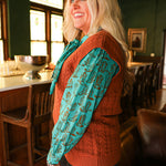 Woman with blonde hair standing in a side profile position wearing the Kodi Vest in a lifestyle scene. The focal point of this image is the sleeveless top and cable knit pattern. The model paired this top with dark-wash denim jeans. 