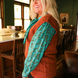 Woman with blonde hair standing in a side profile position wearing the Kodi Vest in a lifestyle scene. The focal point of this image is the sleeveless top and cable knit pattern. The model paired this top with dark-wash denim jeans. 