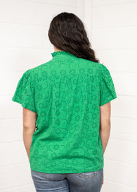Woman with dark hair standing in a back profile position wearing the Lilly Top against a white background. The focal point of this image is the intricate fabric details and green color. The model paired this top with dark-wash denim jeans. 