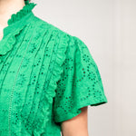 Woman with dark hair standing in front profile position wearing the Lilly Top against a white background. The focal point of this image is a close-up on the green fabric detail.