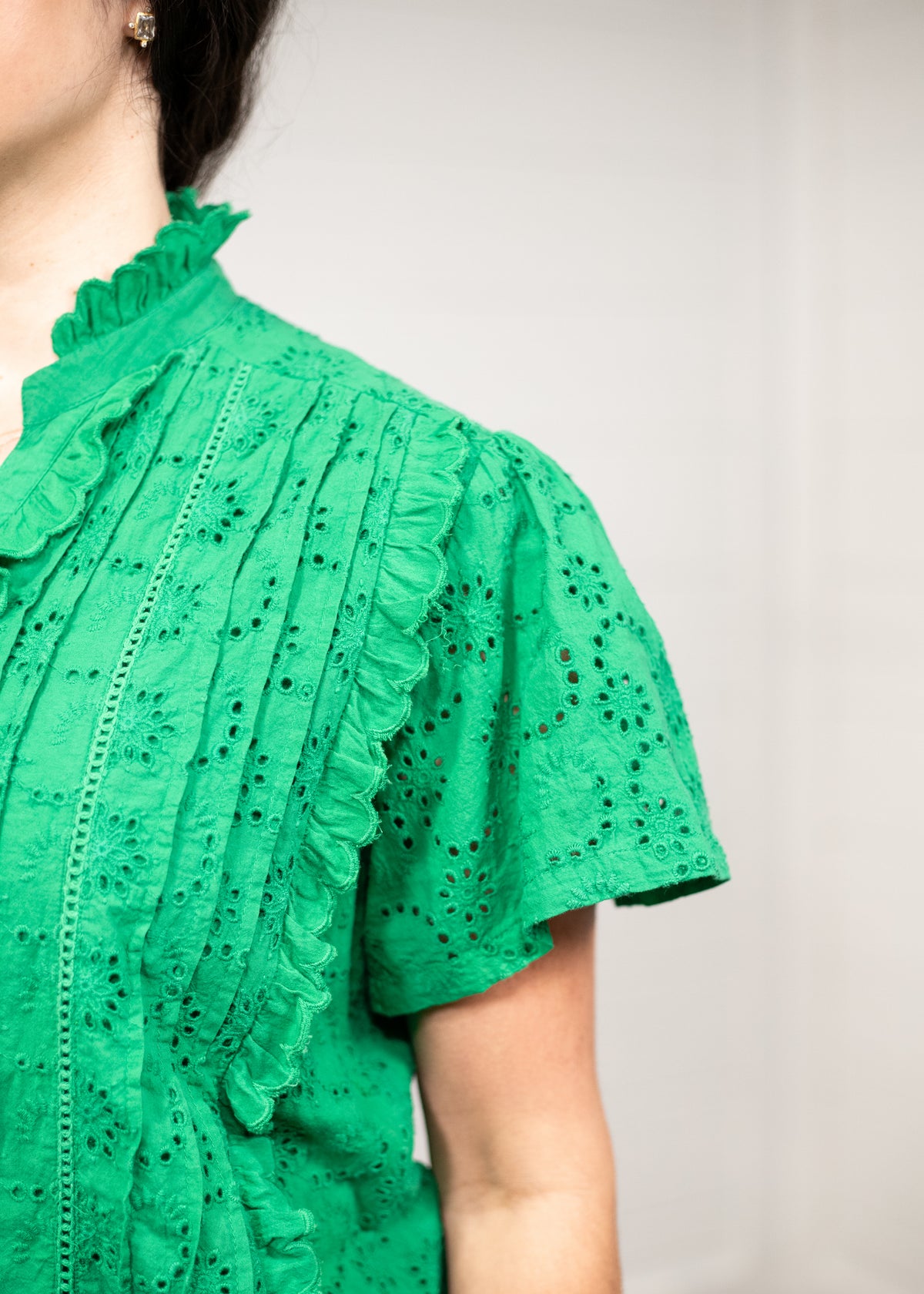 Woman with dark hair standing in front profile position wearing the Lilly Top against a white background. The focal point of this image is a close-up on the green fabric detail.