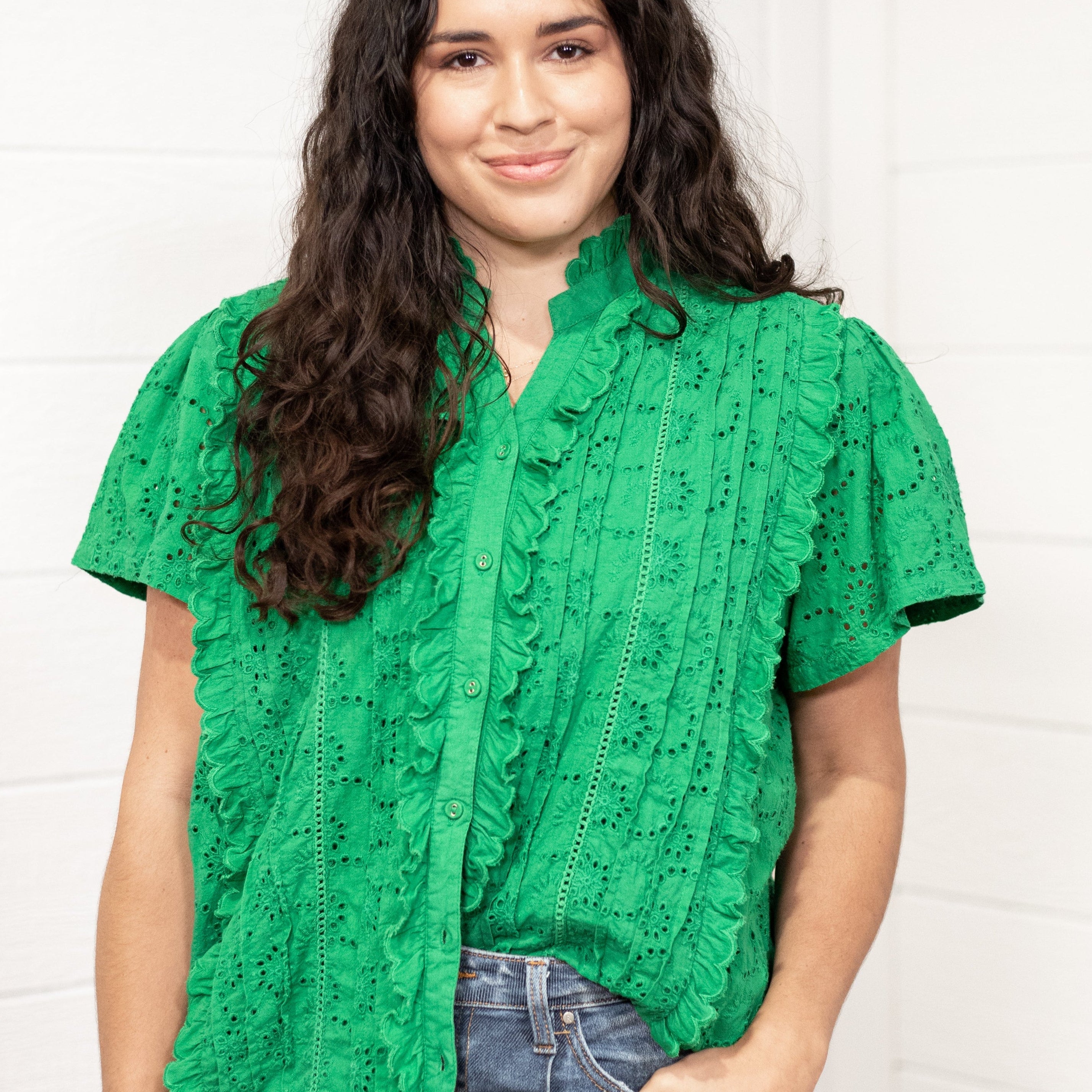 Woman with dark hair standing in a front profile position wearing the Lilly Top against a white background. The focal point of this image is the intricate details of fabric, ruffles, and bright green color. The model paired this top with dark-wash denim jeans.