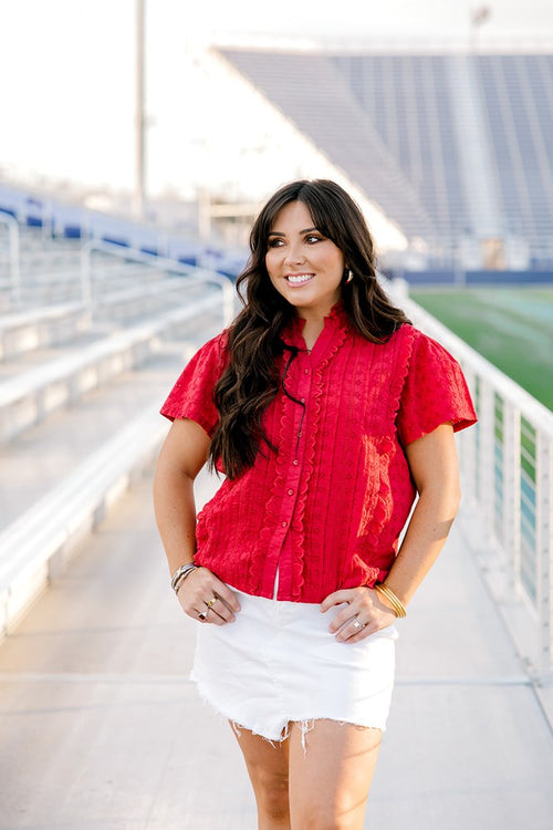 Model with dark hair facing forward wearing a short-sleeve red eyelet top and a white denim skirt. 