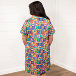 Woman with dark hair standing in a back profile position wearing the Lindsey Dress with a white background. The focal point of this image is the graphics on the back of the dress with slight emphasis on the collar and back of sleeves. 