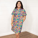 Woman with dark hair standing in a front profile position wearing the Lindsey Dress against a white background. The focal point of this image is the entirety of the dress with graphics visible. The model paired this dress with white and gold sneakers. 