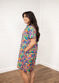 Woman with dark hair standing in a side profile position wearing the Lindsey Dress with a white background. The focal point of this image is the side graphics of the dress with emphasis on the sleeves. 