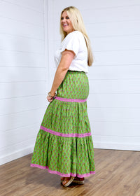 Woman with blonde hair in side profile position wearing the Madison Maxi Skirt against a white background. The images focal point is the side of skirt, expressing it's length and embroidery embellishments on the sides. Model paired with white top and brown sandals.
