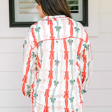 Woman with dark hair wearing a long-sleeve pajama top and pants set that features green, red, and pink bow graphics. 