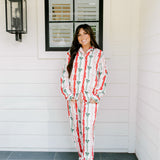Woman with dark hair wearing a long-sleeve pajama top and pants set that features green, red, and pink bow graphics. 