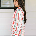 Woman with dark hair wearing a long-sleeve pajama top and pants set that features green, red, and pink bow graphics. 