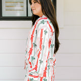 Woman with dark hair wearing a long-sleeve pajama top and pants set that features green, red, and pink bow graphics. 