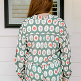 Woman with red hair wearing a long-sleeve top and long pant pajama set. The Pajamas feature fun red & green Christmas icon graphics. 