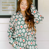 Woman with red hair wearing a long-sleeve top and long pant pajama set. The Pajamas feature fun red & green Christmas icon graphics. 
