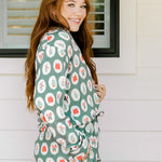 Woman with red hair wearing a long-sleeve top and long pant pajama set. The Pajamas feature fun red & green Christmas icon graphics. 