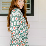 Woman with red hair wearing a long-sleeve top and long pant pajama set. The Pajamas feature fun red & green Christmas icon graphics. 