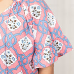 Woman with dark hair standing in a front profile position wearing the Mia Top against a white background. The focal point of this image is the sleeve details (pleating, and tassels). 