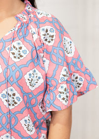 Woman with dark hair standing in a front profile position wearing the Mia Top against a white background. The focal point of this image is the sleeve details (pleating, and tassels). 
