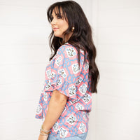 Woman with dark hair standing in a side profile position wearing the Mia Top against a white background. The focal point of this image is the unique pink and blue graphics. The model paired this top with light-wash denim jeans.