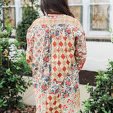 Woman with dark hair standing in a back profile position wearing the Nina Top in a lifestyle scene. The focal point of this image is the red/blue patchwork. The model paired this top with light-wash denim jeans.