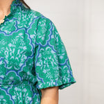 Woman with dark hair standing in a front profile position wearing the Nova Dress against a white background. The focal point of this image is the close-up detail of graphics on the dress. 