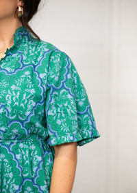 Woman with dark hair standing in a front profile position wearing the Nova Dress against a white background. The focal point of this image is the close-up detail of graphics on the dress. 