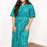 Woman with dark hair standing in a front profile position wearing the Nova Dress against a white background. The focal point of this image is the front details on dress (ruffle down buttons, belt). 