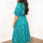 Woman with dark hair standing in a side profile position wearing the Nova Dress against a white background. The focal point of this image is the graphics on the dress as well as the sleeve length and belt. 