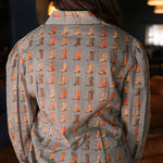 Woman with dark hair standing in a back profile position wearing the Oakley Top in a lifestyle scene. The focal point of this image is the boot graphics. The model paired this top with light-wash denim jeans. 