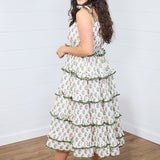 Woman with dark hair standing in side profile position wearing the Paloma Dress against a white background. The focal point of this image is the side ruffles of the dress, the length, and graphics. The model paired this dress with cream heels. 