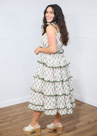 Woman with dark hair standing in side profile position wearing the Paloma Dress against a white background. The focal point of this image is the side ruffles of the dress, the length, and graphics. The model paired this dress with cream heels. 