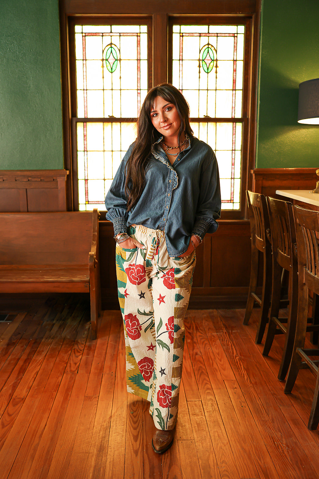 Woman with dark hair wearing the Pendleton Pants featuring stars embellishments, red rose graphics, and aztec print down side of pants. 