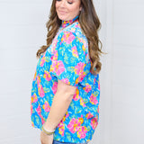 Woman with dark hair standing in a side profile position wearing the Reece Top against a white background. The focal point of this image is the sleeve length and the white embroidery across the shoulders. The model paired this top with dark-wash denim shorts.