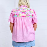 Woman with blonde hair standing in a back profile position wearing the Reece against a white background. The focal point of this image is the embroidery across the shoulders and pleating down the back of the top. The model paired this top with a light-wash denim skirt.